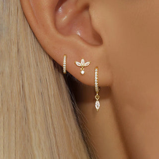 Close-up of an ear wearing gold hoop earrings with small diamonds and a floral earring.